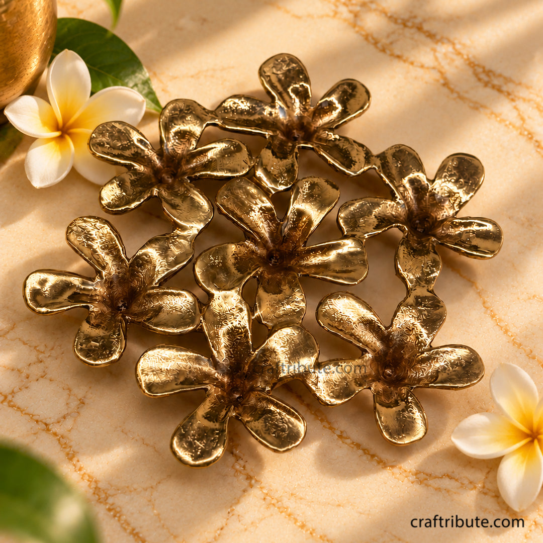 Handcrafted brass Champa flower coaster featuring seven intricately detailed floral elements with an antique gold finish, styled on cream marble with fresh Champa flowers and green leaves.