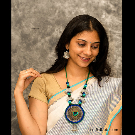 A lady wearing a white chanderi saree with an attractive necklace with black, blue, and green cotton beads and silver earrings