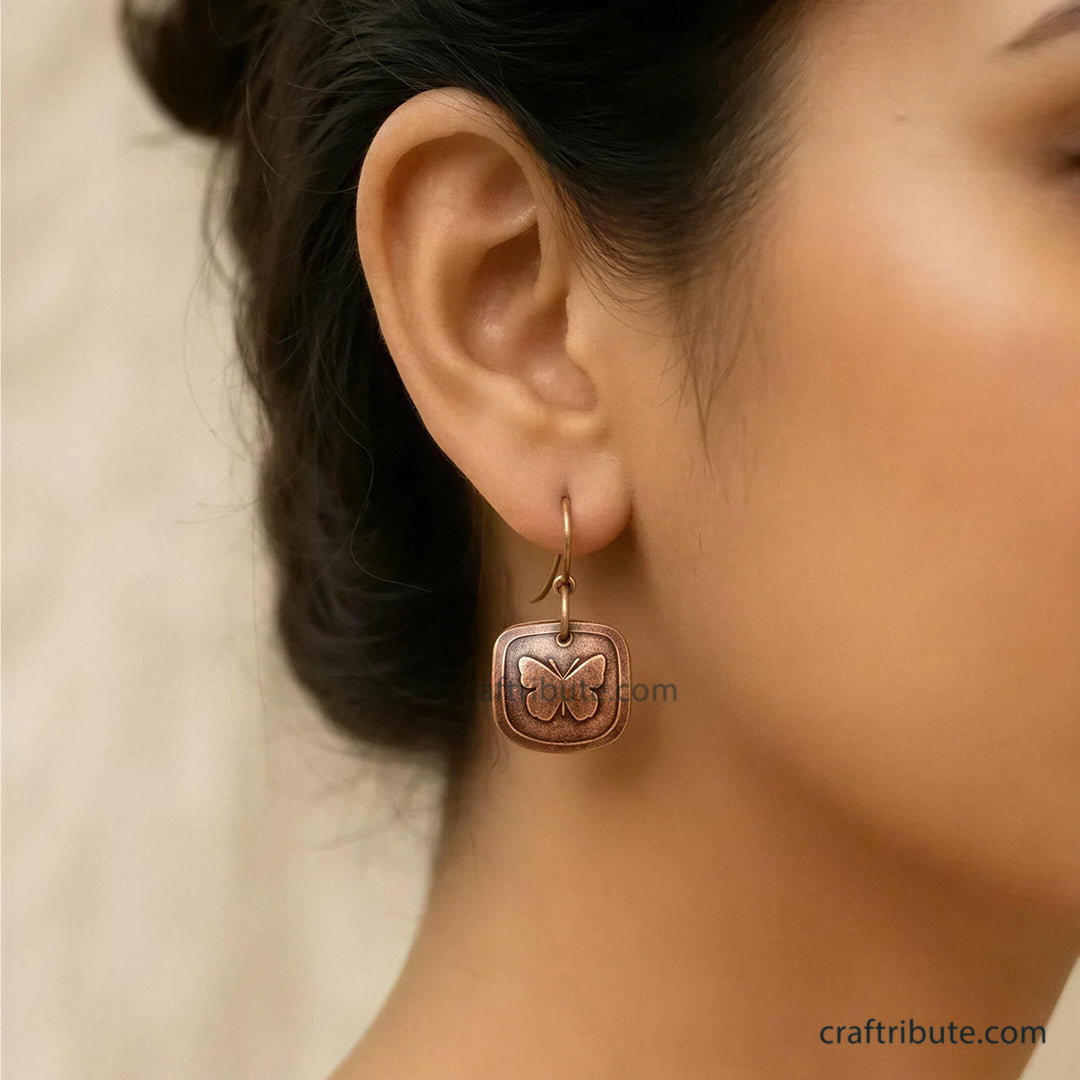 Model wearing handcrafted copper drop earring with a butterfly design etched on it