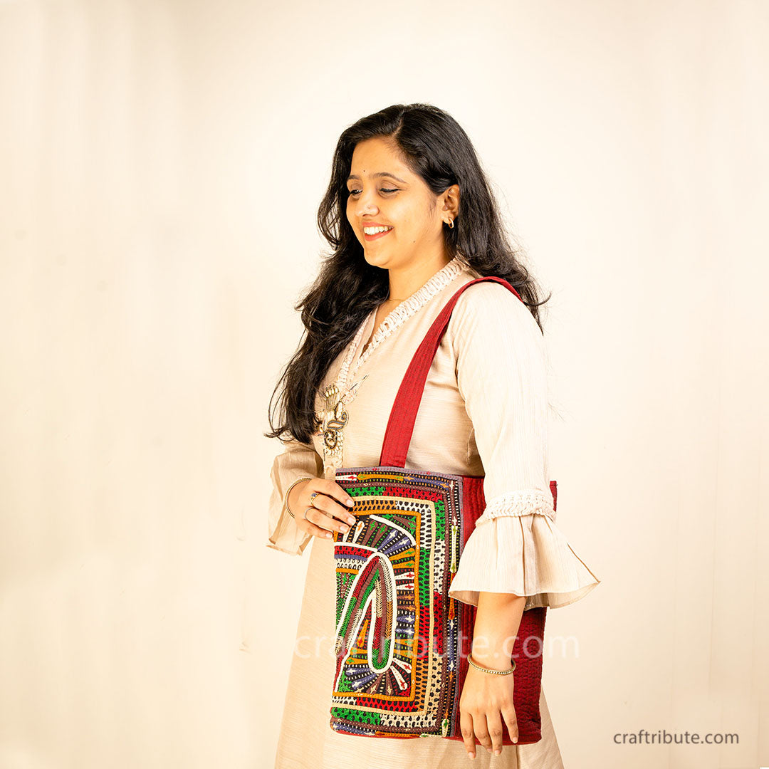 Girl flaunting a red tote bag with Khudi Seba Kutch Embroidery with colourful design
