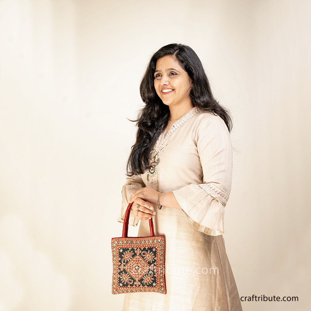 Girl showcasing a handbag with Scorpio (Vicchi) design in Kutch 'Neran' Embroidery style, in bright Red & Gold colours