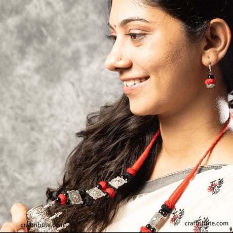 A lady wearing a decorative necklace with an attractive silver pendant and earrings with red and black beads