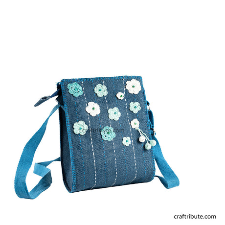 Front side of a hand embroidered blue jute sling bag with light blue and white crochet flowers 