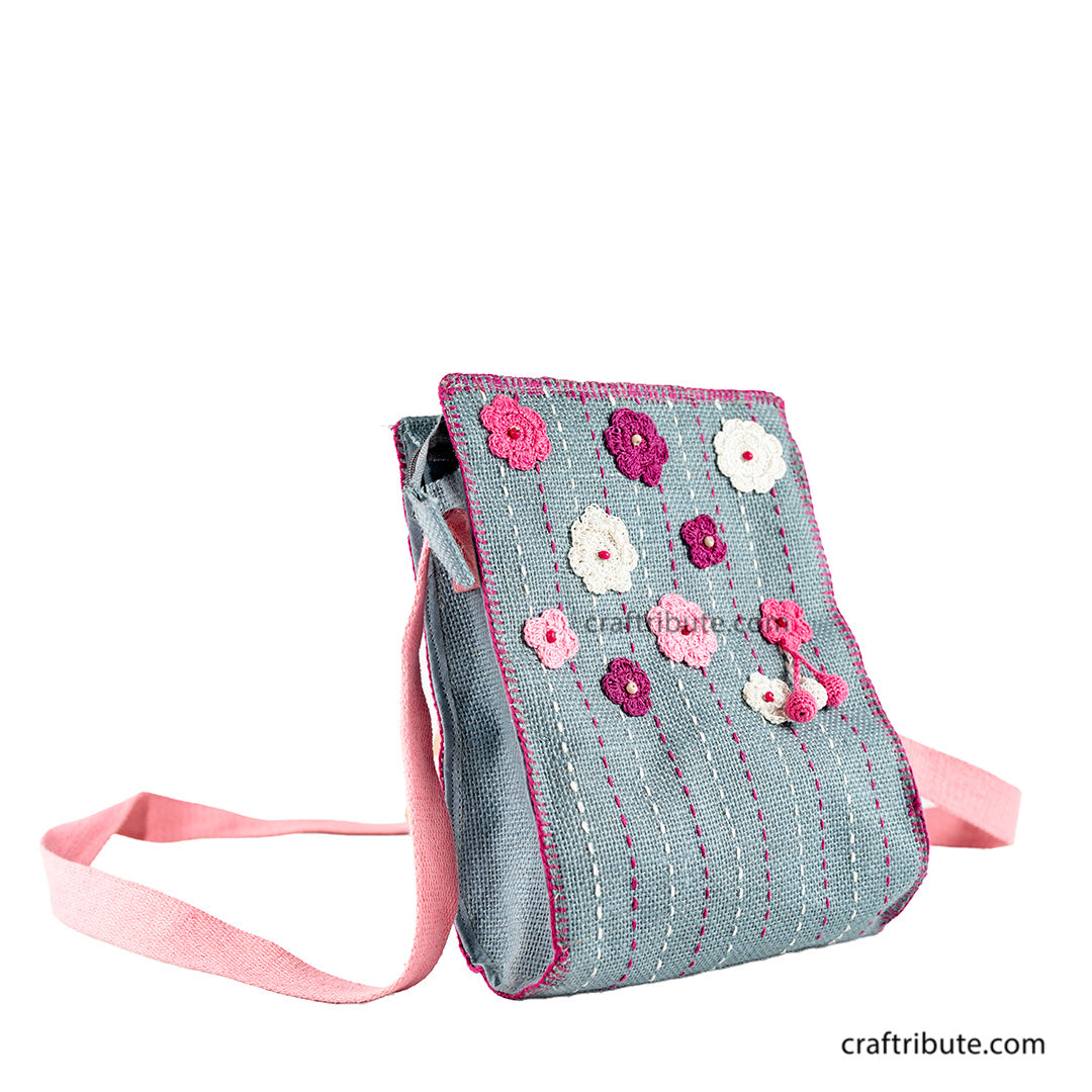 Front side of a hand embroidered grey jute sling bag with crochet pink & white flowers