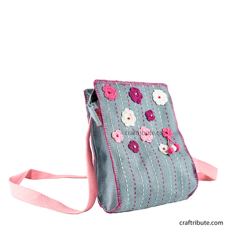 Front side of a hand embroidered grey jute sling bag with crochet pink & white flowers