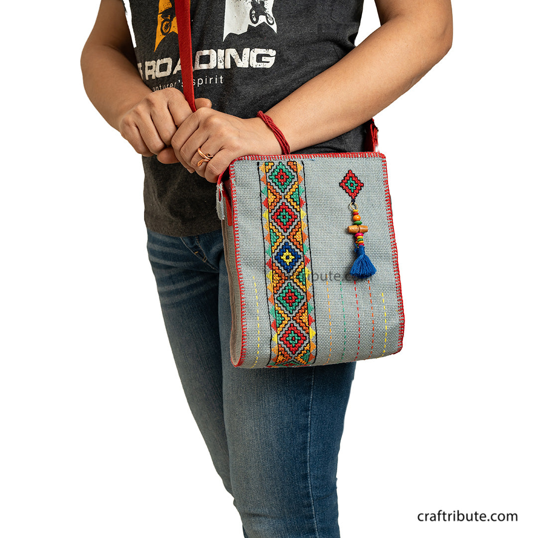 A model carrying a hand embroidered jute sling bag in Grey with red belt