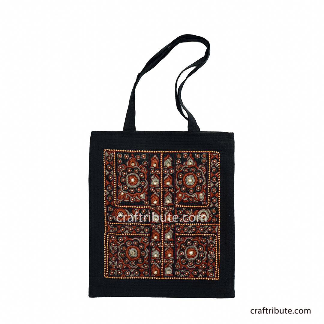 Front side of a tote bag embellished with Sindhi Memon style of Kutch hand embroidered in Black & Orange colours