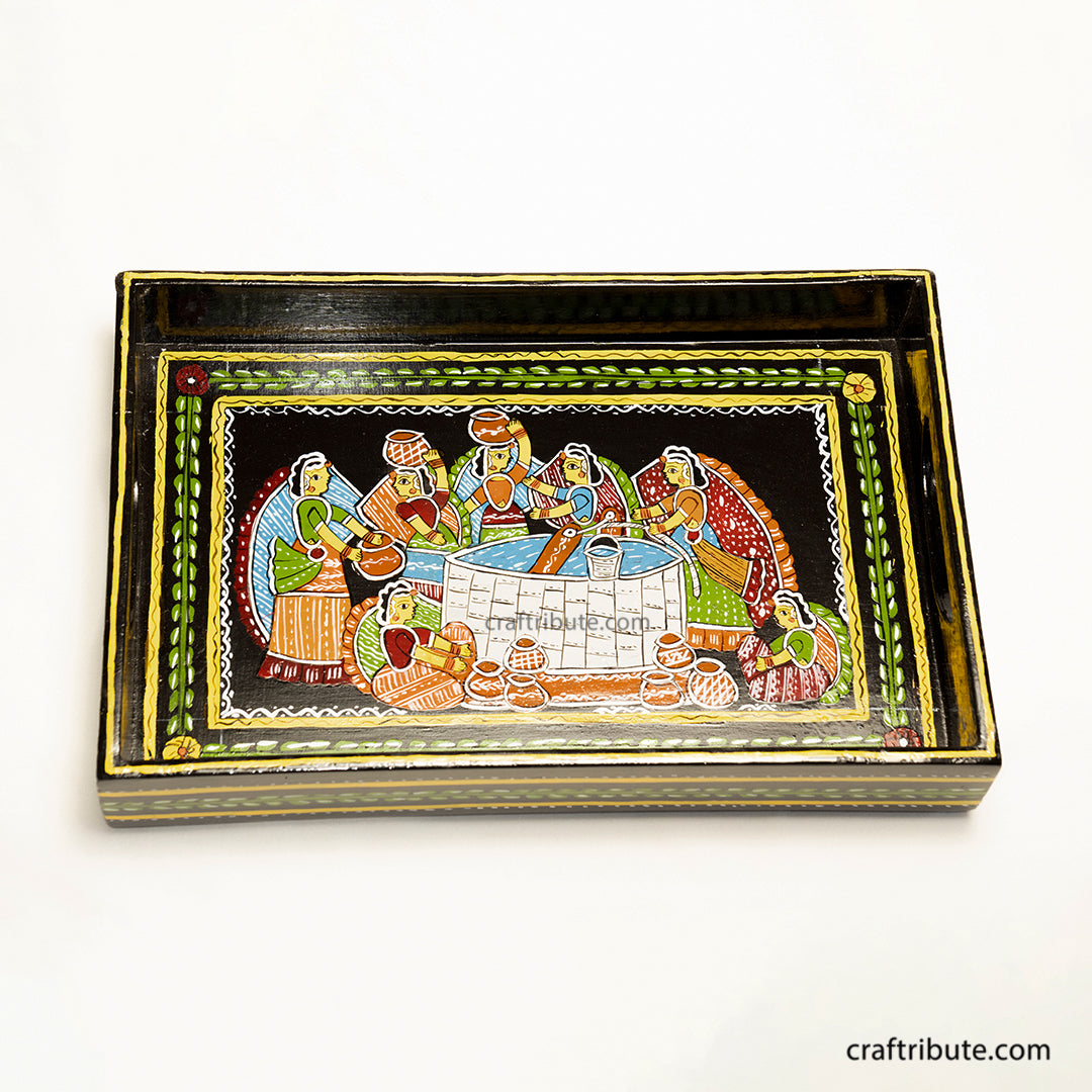 Close up of a wooden tray depicting women gathered around the well to draw water. Hand painted by Tikuli Artists from Bihar in bright colours on a black surface