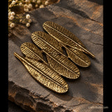 Handcrafted brass Champa leaf coaster featuring intricate leaf-vein detailing and an antique gold finish, arranged on a rustic dark stone surface with delicate white flowers in the background.