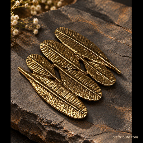 Handcrafted brass Champa leaf coaster featuring intricate leaf-vein detailing and an antique gold finish, arranged on a rustic dark stone surface with delicate white flowers in the background.