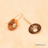 Two handmade oval drop earrings displayed on a warm beige textured background. One earring highlights the front side, and the other highlights the back side