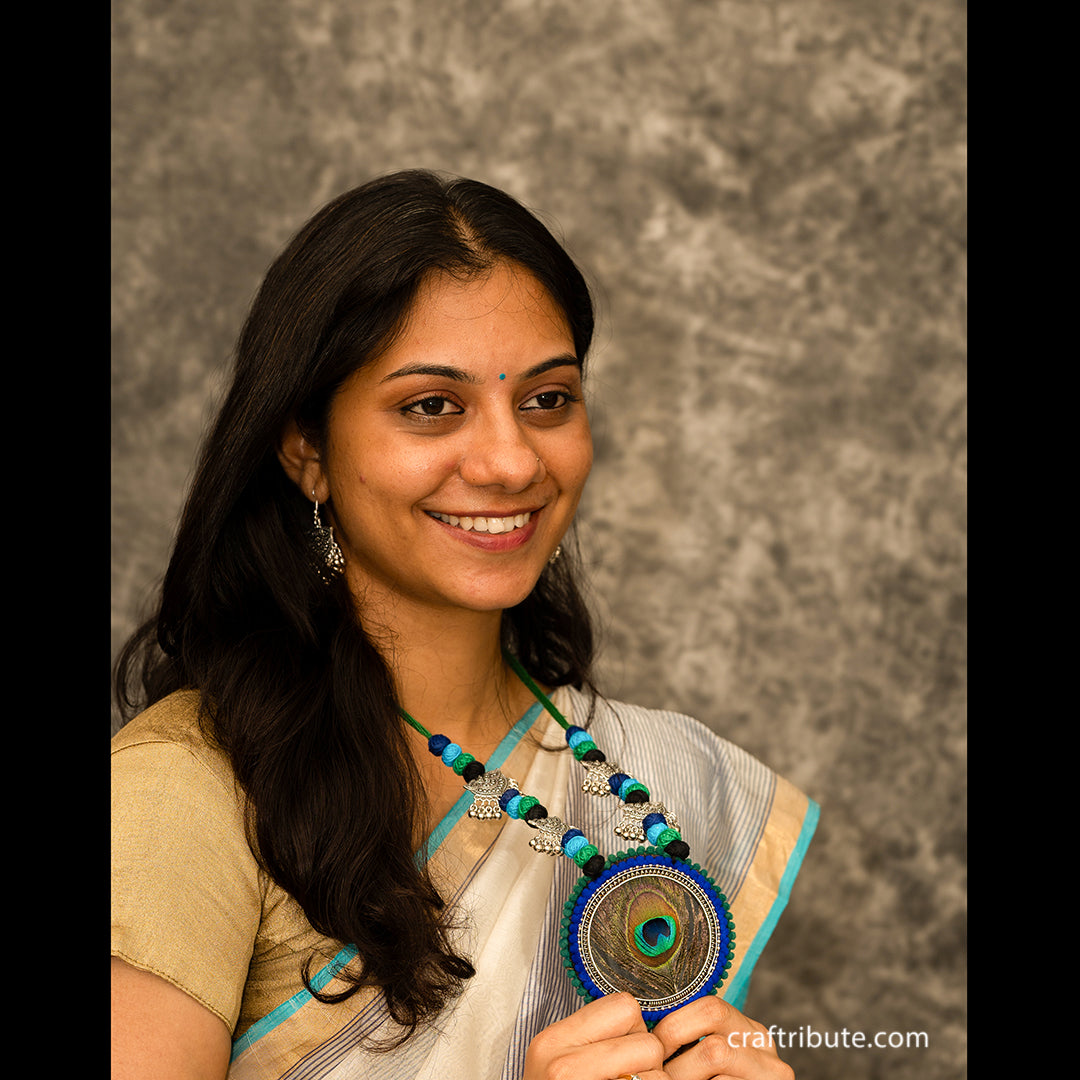 A lady flaunting her attractive neck piece, with a peacock feather pendant 