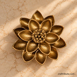 Handcrafted antique brass lotus flower décor with intricately textured layered petals and a detailed centre, photographed from above on a warm cream marble surface.