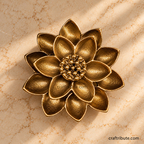 Handcrafted antique brass lotus flower décor with intricately textured layered petals and a detailed centre, photographed from above on a warm cream marble surface.