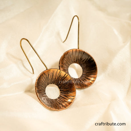 Pair of copper earrings with beautiful texture on a beige fabric background