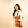 Girl holding a red tote bag with Ahir Kutch Hand embroidery symbolising opulence through its floral design in lilac & Gold