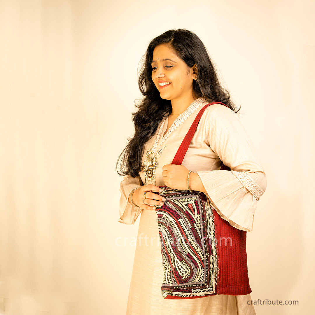 Girl showcasing a red tote bag with Khudi Seba Kutch Embroidery with grey & white design 