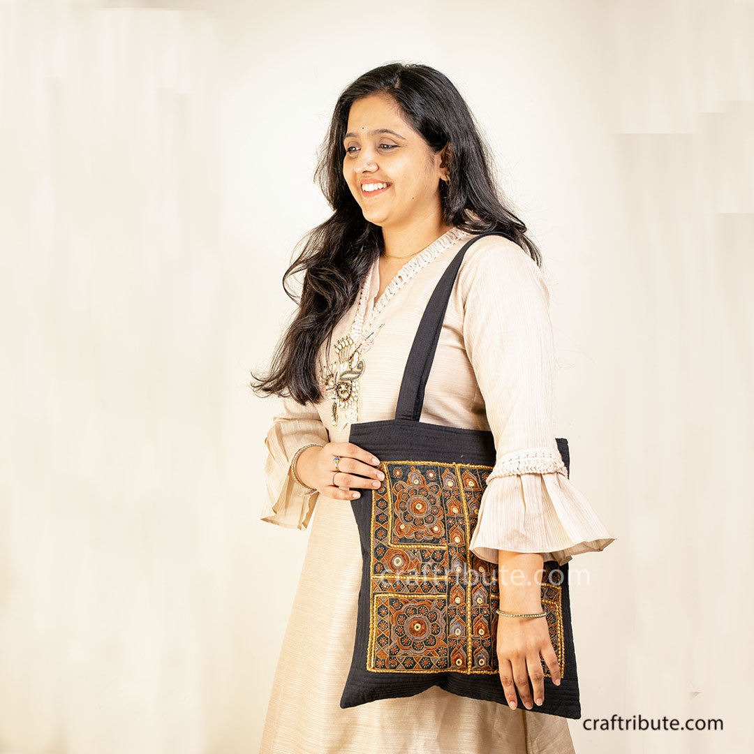 Girl displays a tote bag embellished with Sindhi Memon style of Kutch hand embroidery in Black & Orange colours