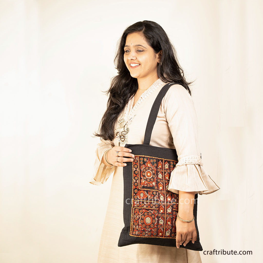 Model carrying a tote bag embellished with Sindhi Memon style of Kutch hand embroidery in Black & Orange colours
