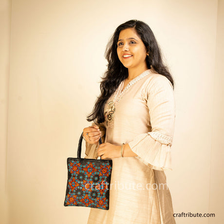 Beautiful black hand bag with Pakko Kutch Hand Embroidery with 9 stars design in Orange & blue held by a girl
