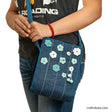 A model carrying a hand embroidered jute sling bag in bue with light blue and white crochet flowers