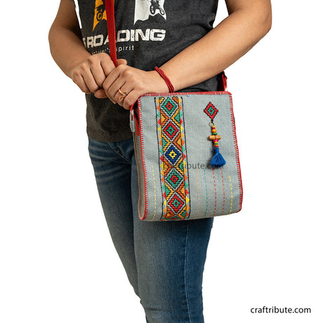 A model carrying a hand embroidered jute sling bag in Grey with red belt