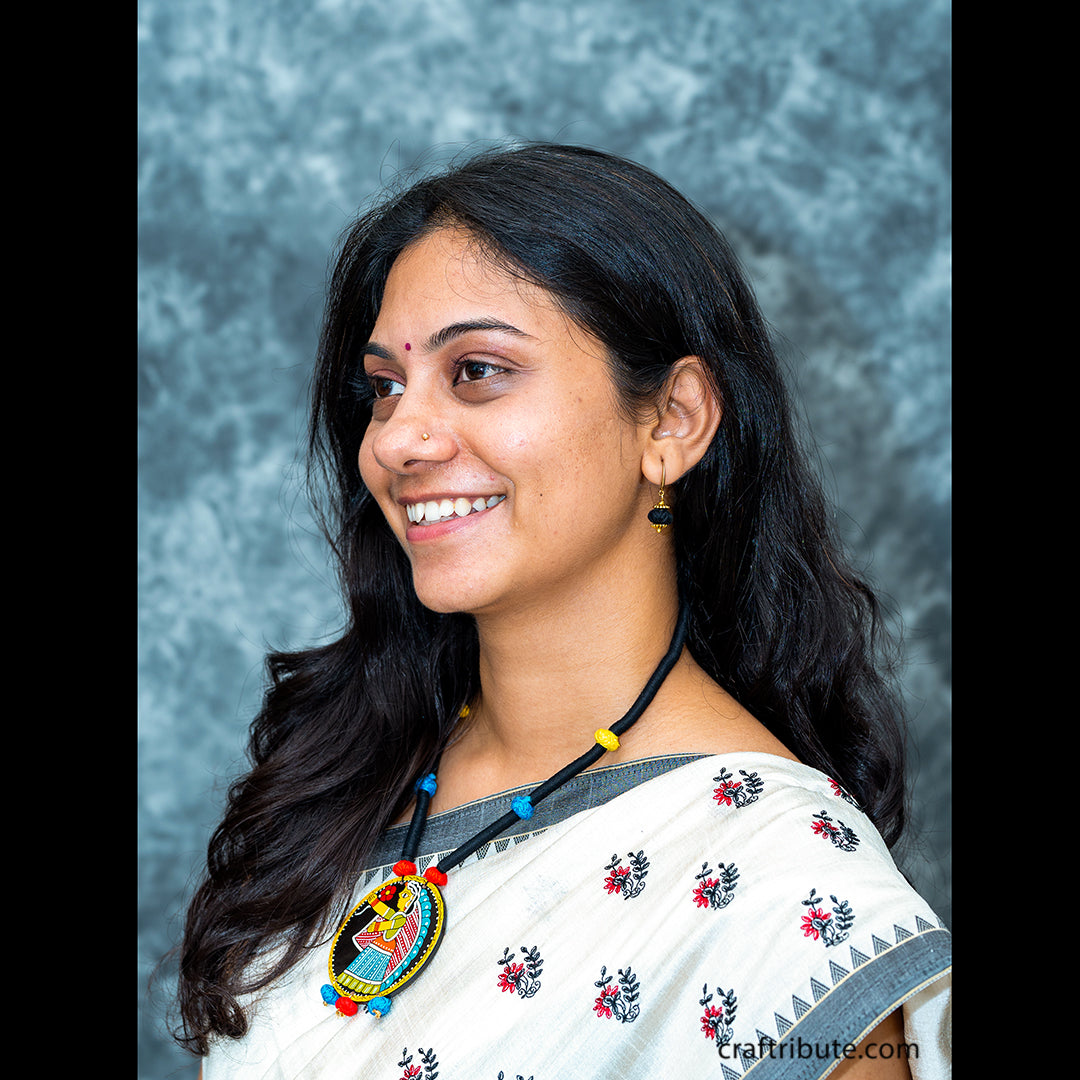 A lady showcasing a black thread necklace with a hand-painted Tikuli Art pendant with colourful beads 