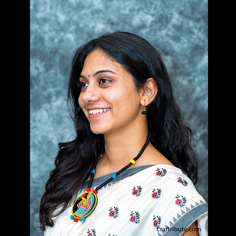 A lady showcasing a black thread necklace with a hand-painted Tikuli Art pendant with colourful beads 