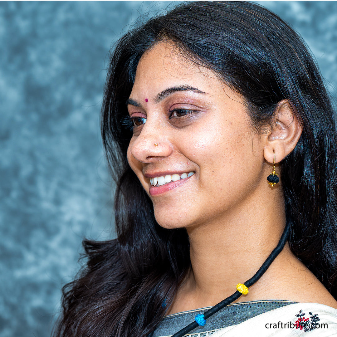 A lady flaunting a black thread necklace with colourful beads, with black cotton bead earring