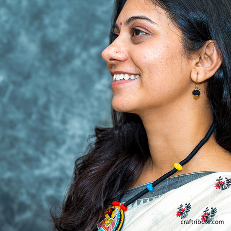 A lady showcasing a black thread necklace with a hand-painted Tikuli Art pendant with black bead earrings
