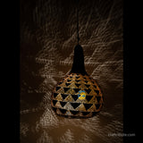 Picture depicts a handcrafted Tumba (dried bottle gourd) lamp from Bastar, Chhattisgarh with triangle design, lit at night creating beautiful shadows on the wall