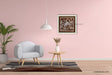 A beautiful framed square Warli painting hangs on a light pink wall in a modern living room mockup with a gray armchair, side table, and hanging lamp.