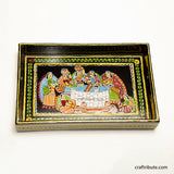 Close up of a wooden tray depicting women gathered around the well to draw water. Hand painted by Tikuli Artists from Bihar in bright colours on a black surface